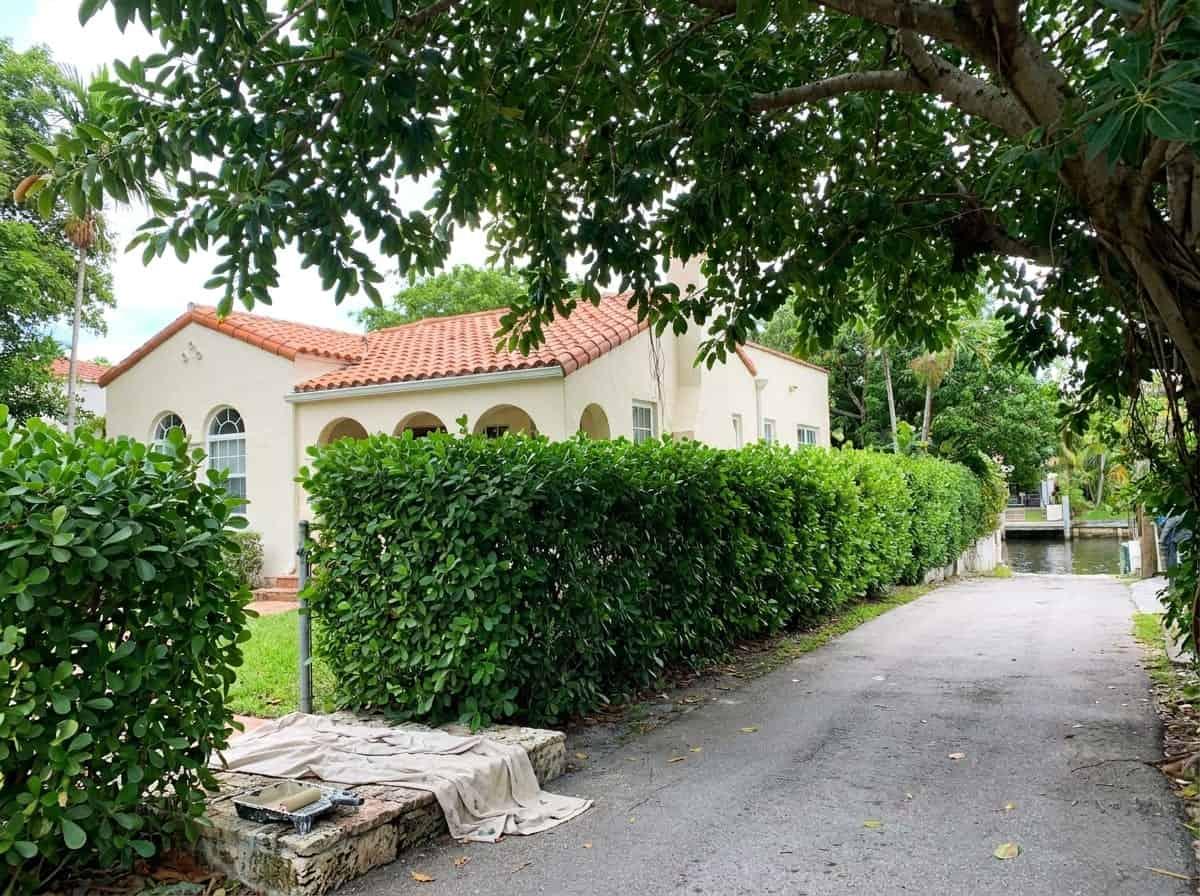 Single-story stucco house behind a clipped hedge in Gulf Stream, FL
